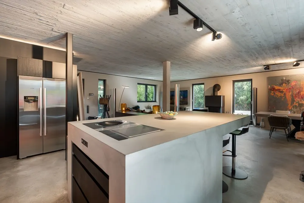Moderne offene Küche mit Kochinsel, Barhockern und Blick ins Wohnzimmer mit großen Fenstern.