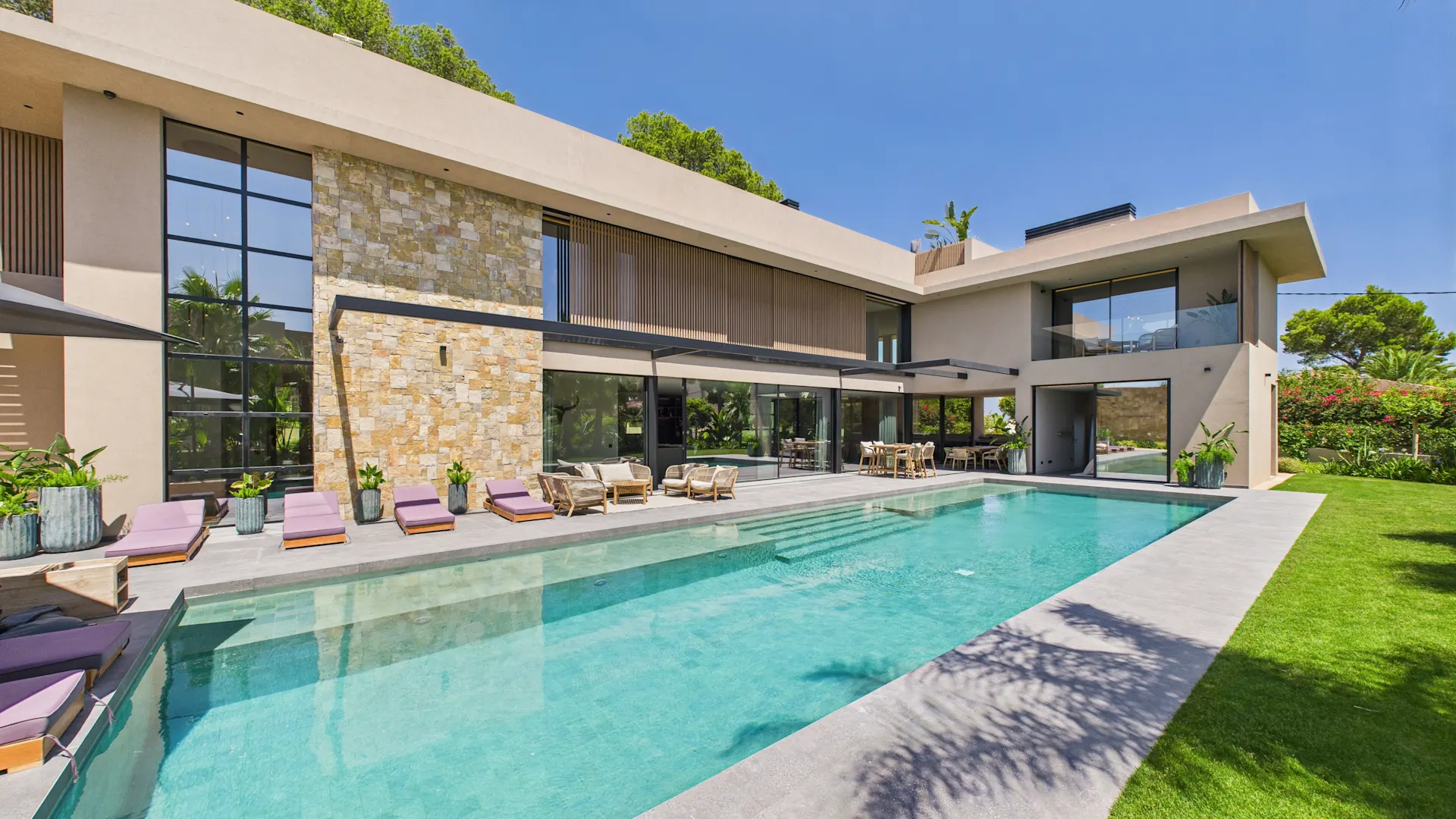Moderne Villa mit großem Pool, Liegestühlen und Terrasse, umgeben von Rasen und Pflanzen.
