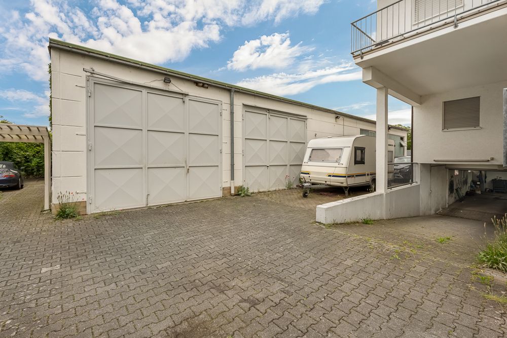 Gepflasterter Innenhof mit Garagentoren, Wohnwagen und Teil eines Wohngebäudes.