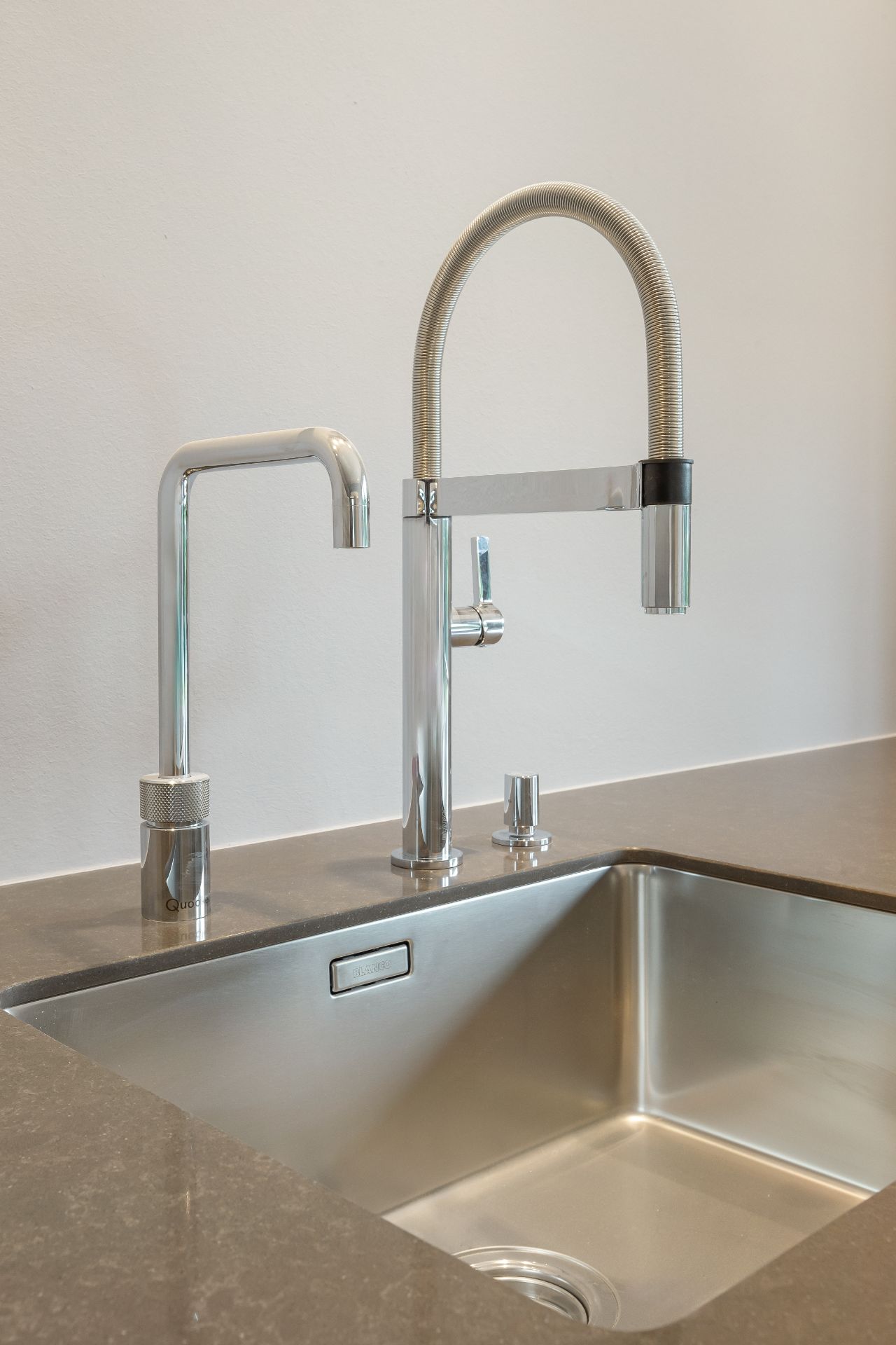 Moderne Edelstahlspüle mit zwei Wasserhähnen auf einer grauen Arbeitsplatte.