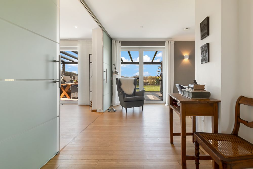 Heller Flur mit Holzboden, Sessel am Fenster und Blick auf Terrasse und Garten.