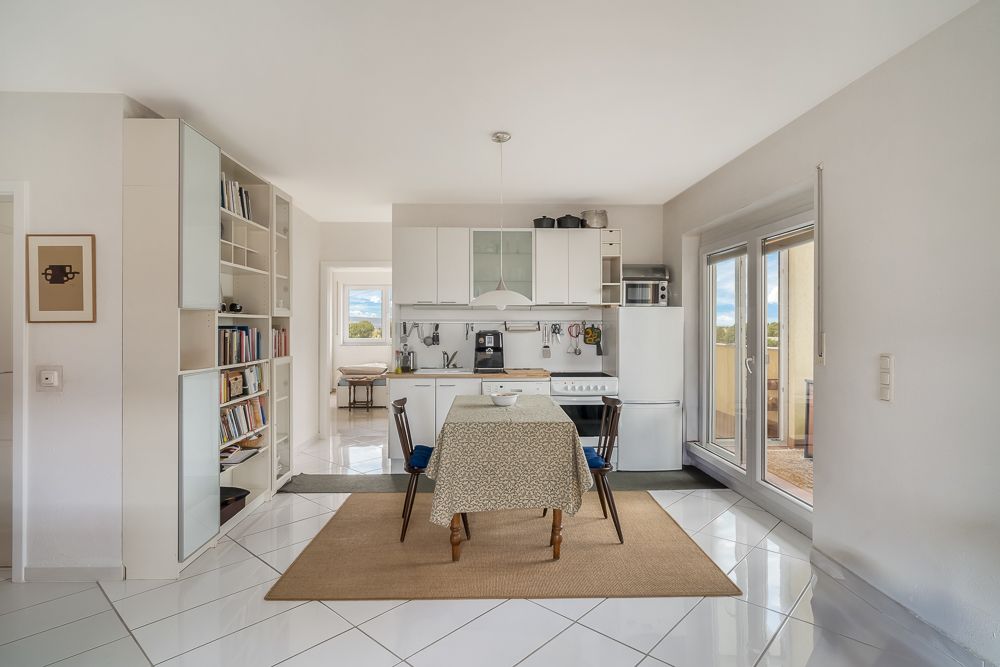 Helle Küche mit Esstisch, vier Stühlen, Bücherregal und Zugang zu einem Balkon.