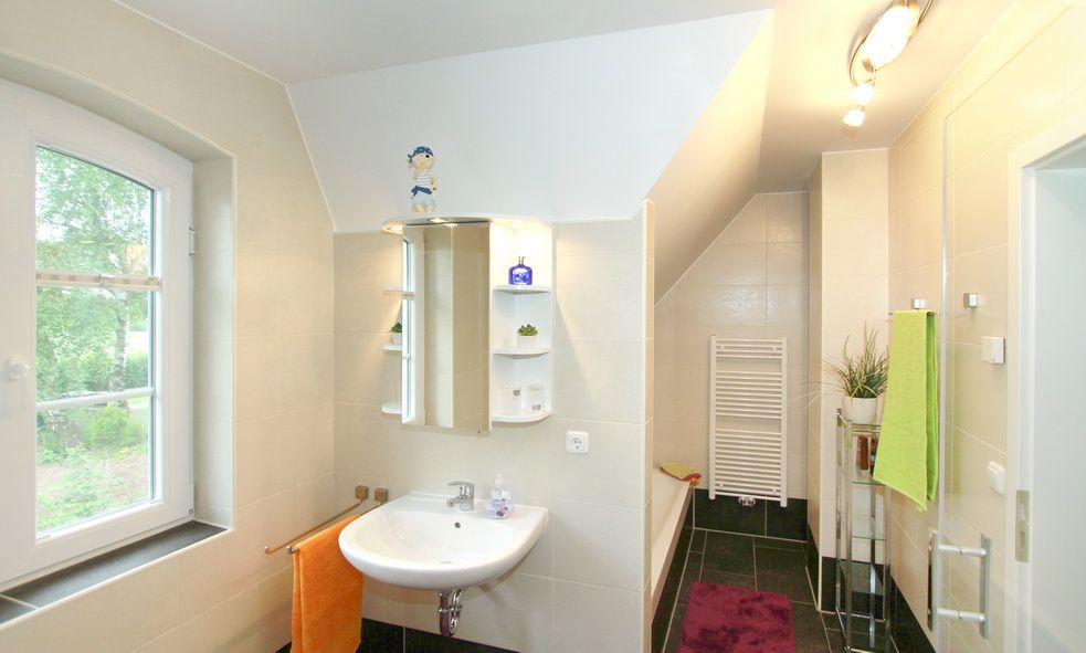 Helles Badezimmer mit Waschbecken, Spiegel, Fenster, Handtuchhalter und Badewanne.