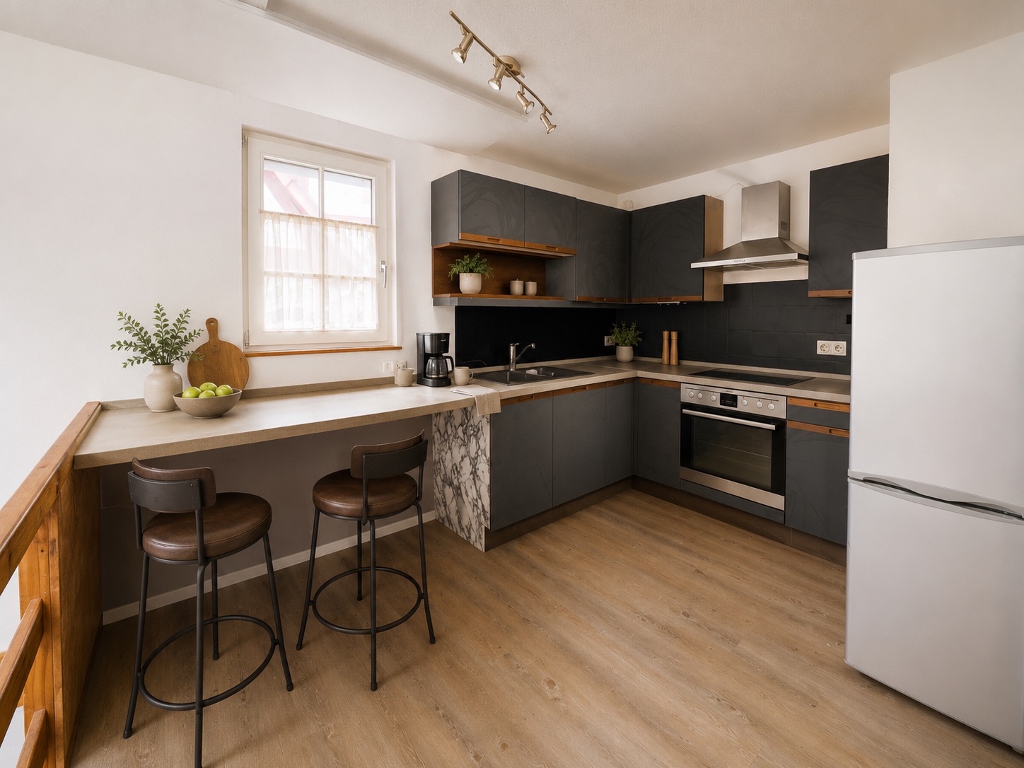 Moderne Küche mit grauen Schränken, Frühstückstheke, zwei Hockern und großem Kühlschrank.