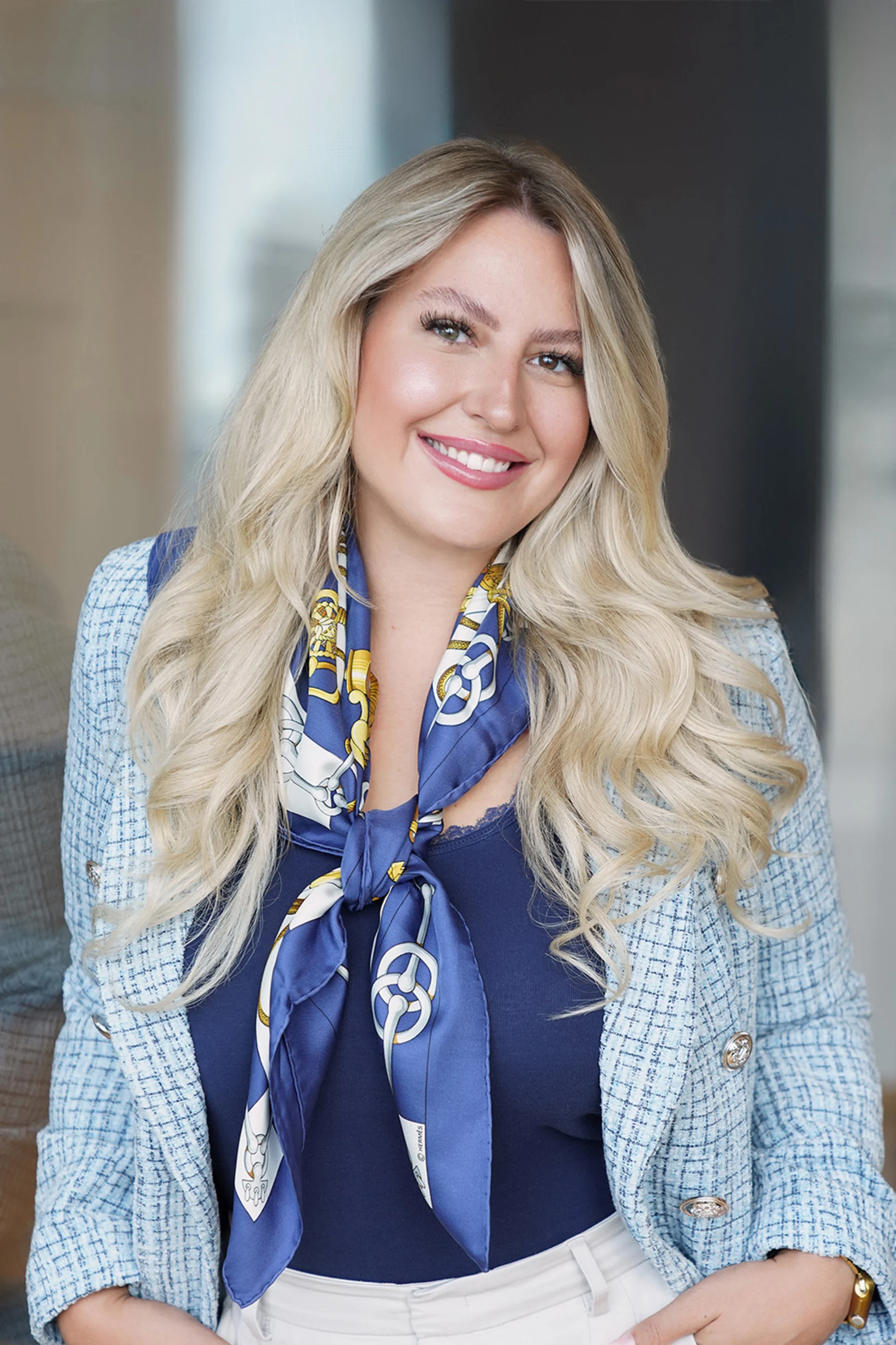 Frau mit blonden langen Haaren, blauem Oberteil und gemusterter blauer Halstuch, lächelt in die Kamera.
