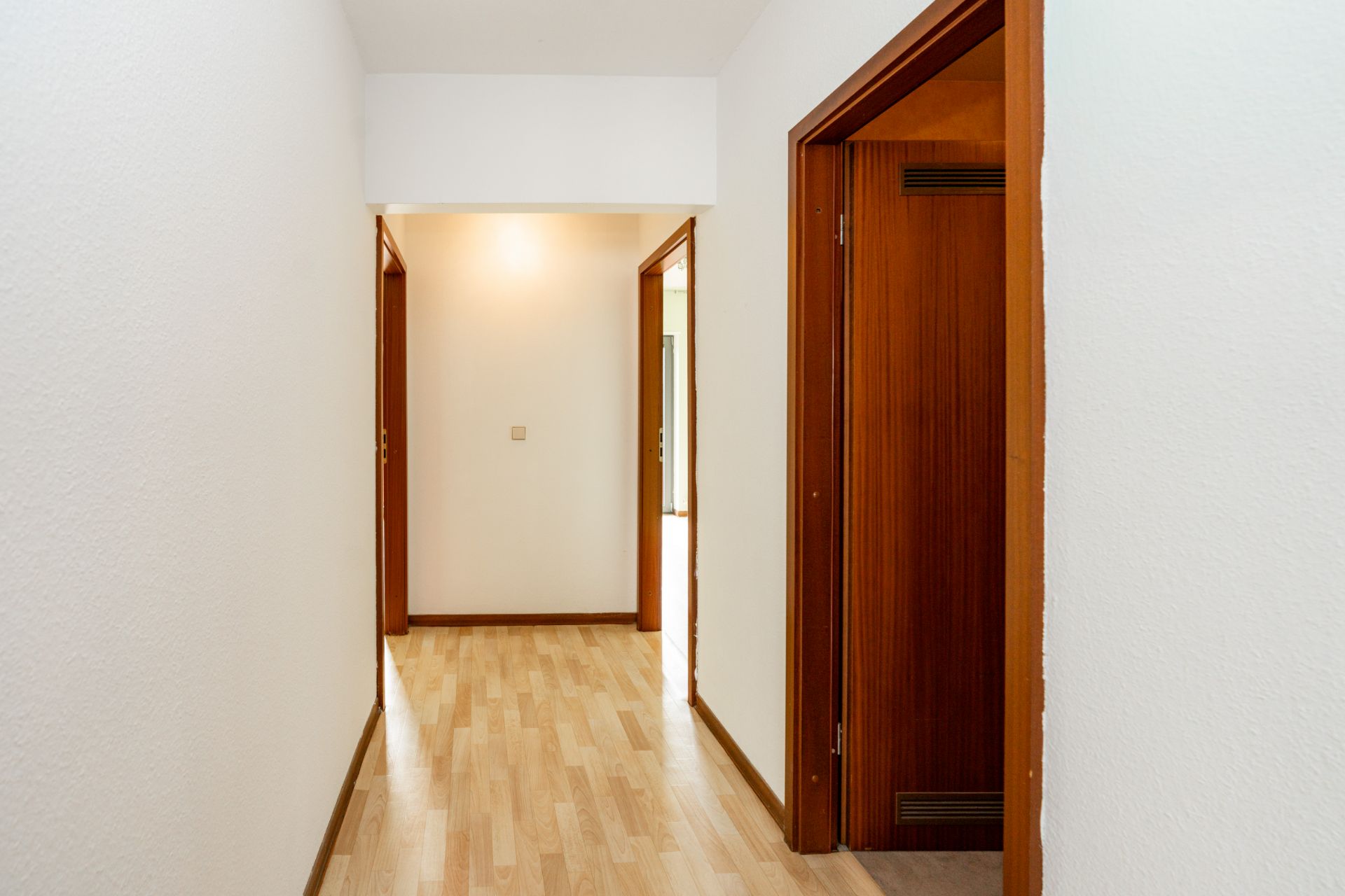 Heller Flur mit Laminatboden und mehreren Türen zu angrenzenden Zimmern.
