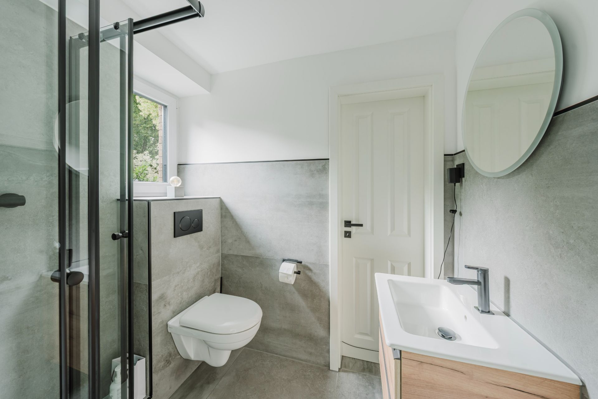 Modernes Bad mit Dusche, wandhängendem WC, Waschbecken und rundem Spiegel.
