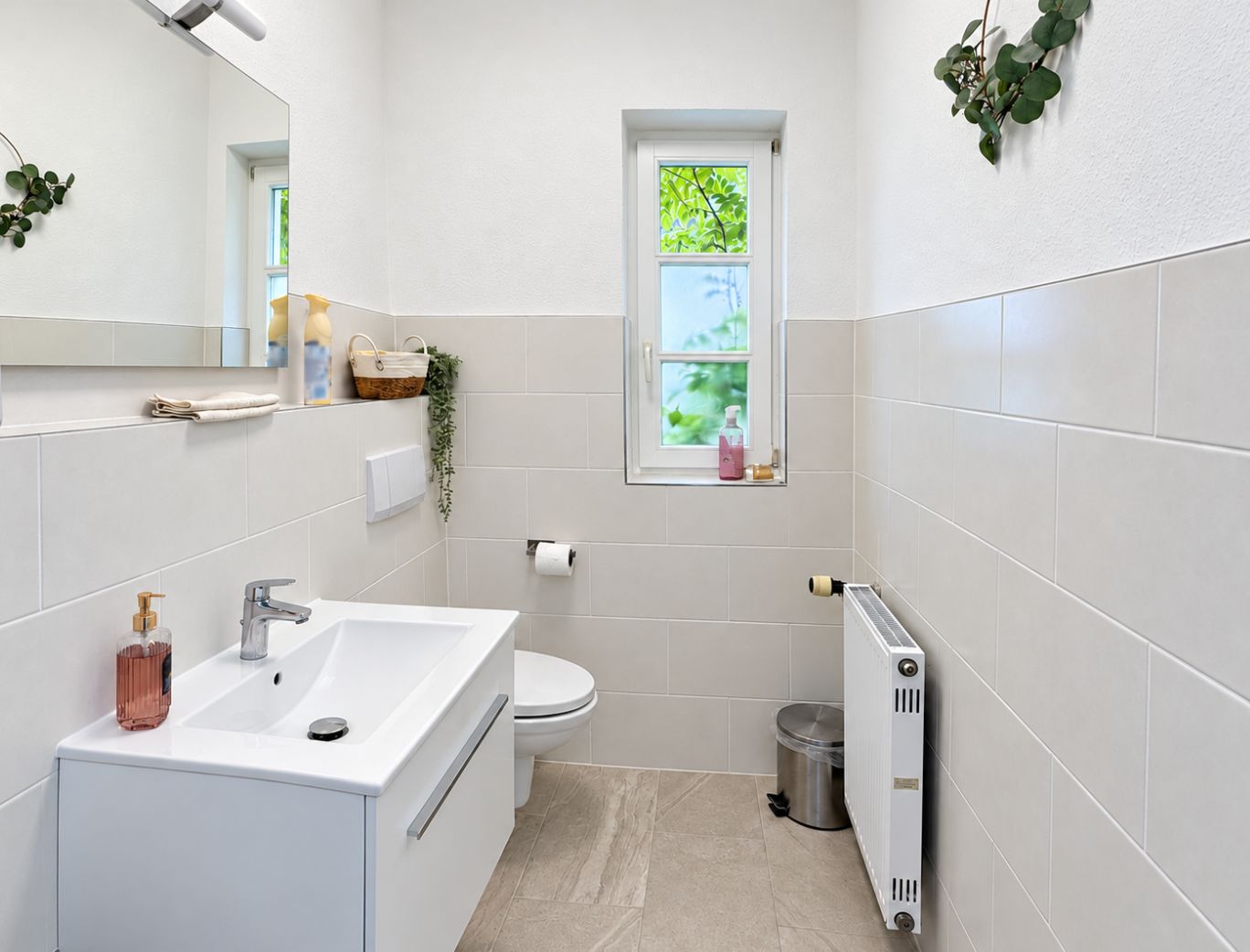 Modernes Badezimmer mit Waschbecken, WC, Fenster und Heizkörper, dekoriert mit Pflanzen.