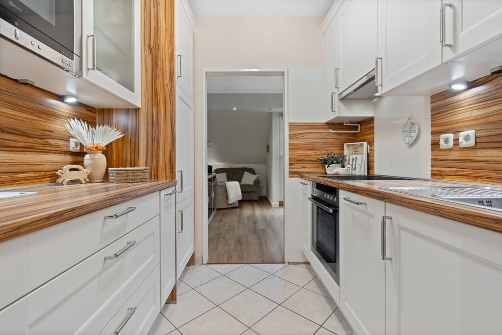Moderne Küche mit weißen Schränken, Holzarbeitsplatten und Blick ins Wohnzimmer.