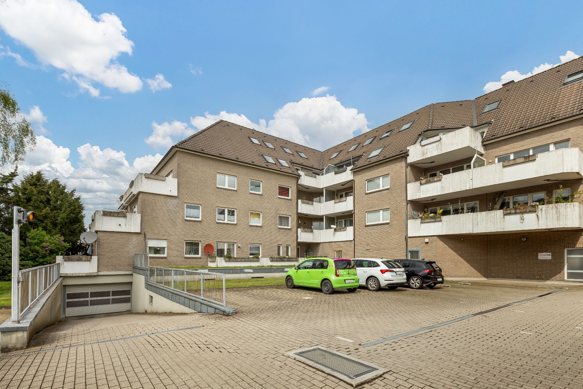 Mehrfamilienhaus mit Balkonen, Parkplätzen und Tiefgaragenzufahrt bei sonnigem Wetter.