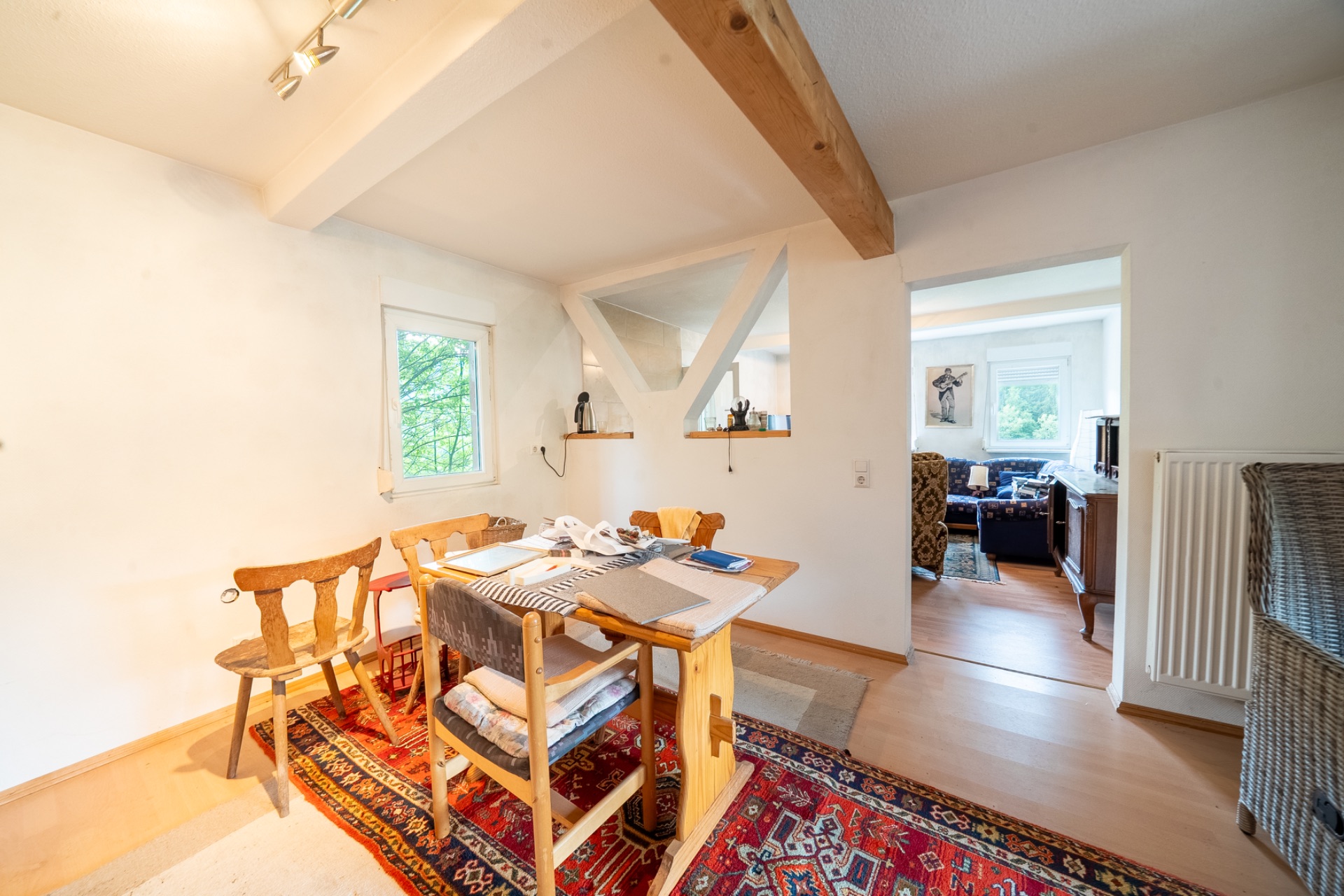 Essbereich mit Holztisch, Stühlen und Teppich, angrenzend an ein Wohnzimmer mit viel Tageslicht.