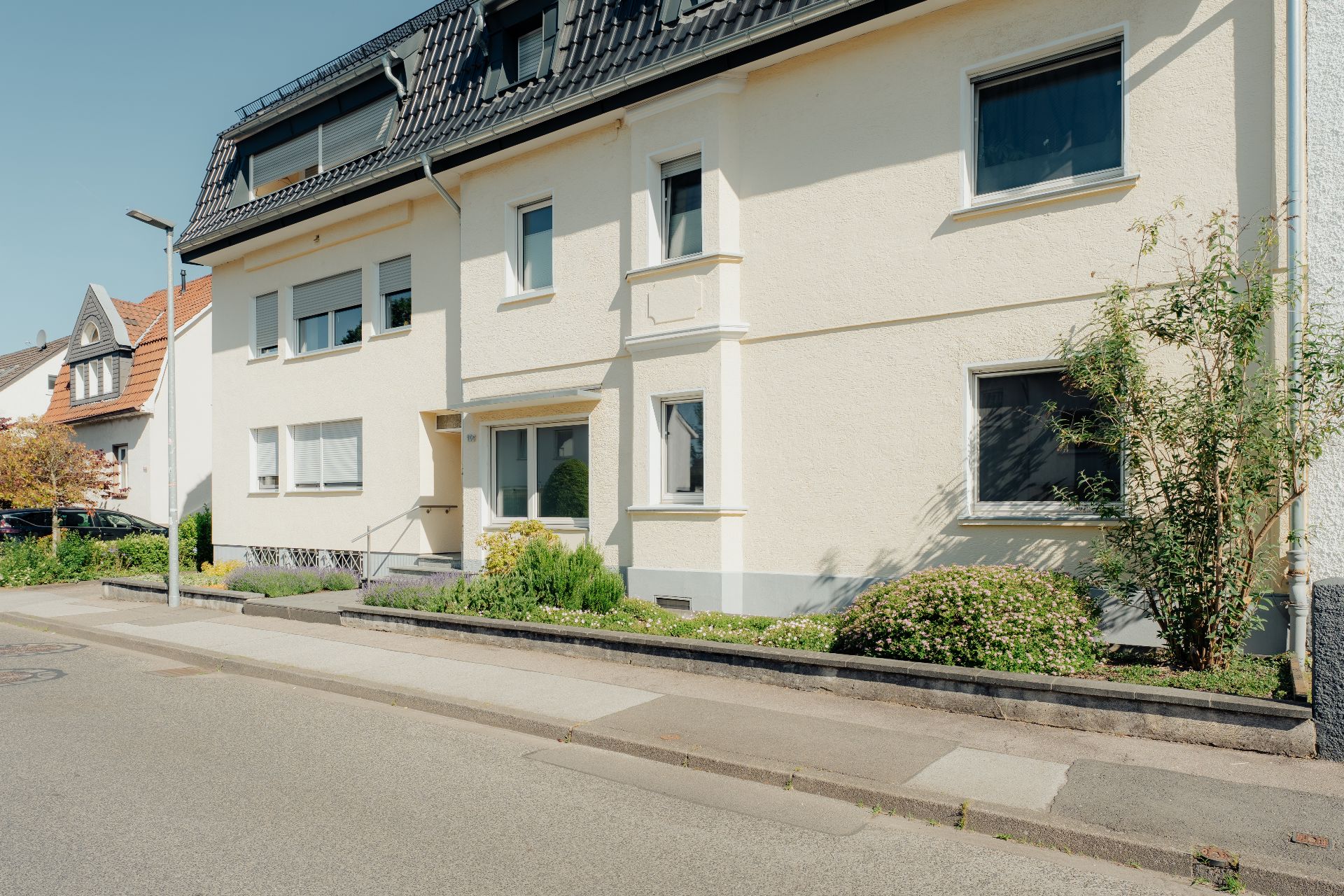 Helles, mehrstöckiges Wohnhaus mit Vorgarten an einer ruhigen Straße.