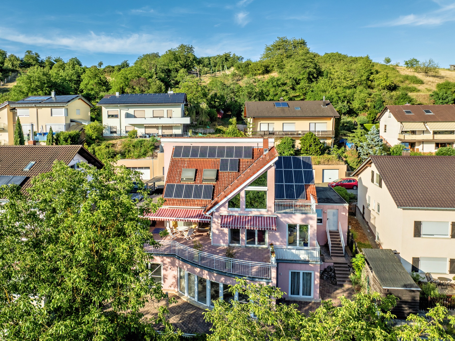 Haus mit Solarpanels auf dem Dach, großer Terrasse und umliegenden Gärten in Wohngegend.