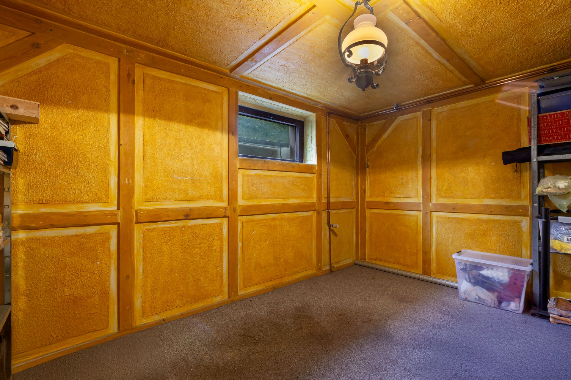 Kleiner Raum mit gelben Holzwänden, Teppichboden, Fenster und Regal mit Kunststoffbox.