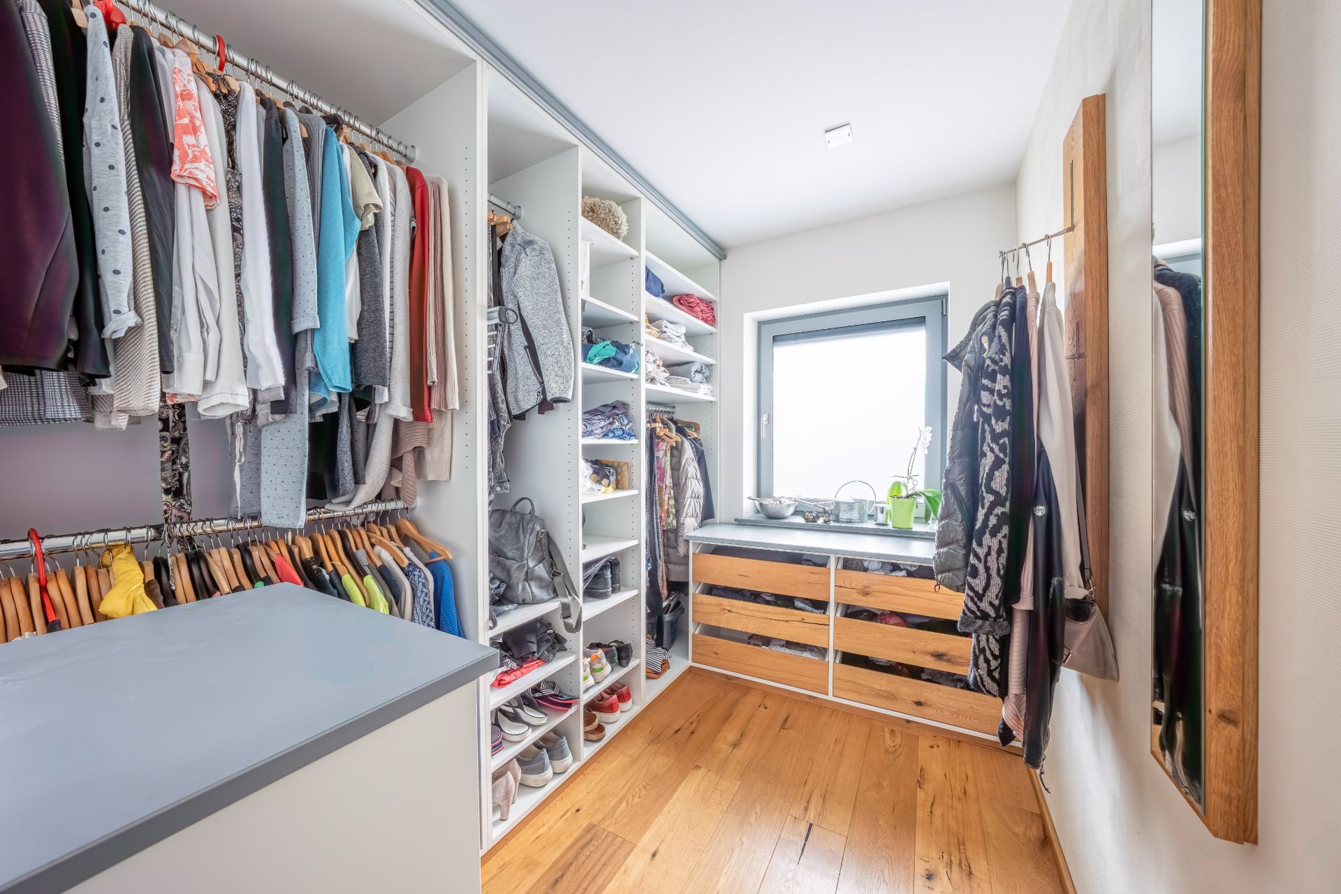 Heller begehbarer Kleiderschrank mit Kleiderstangen, Regalen und Holzfußboden.