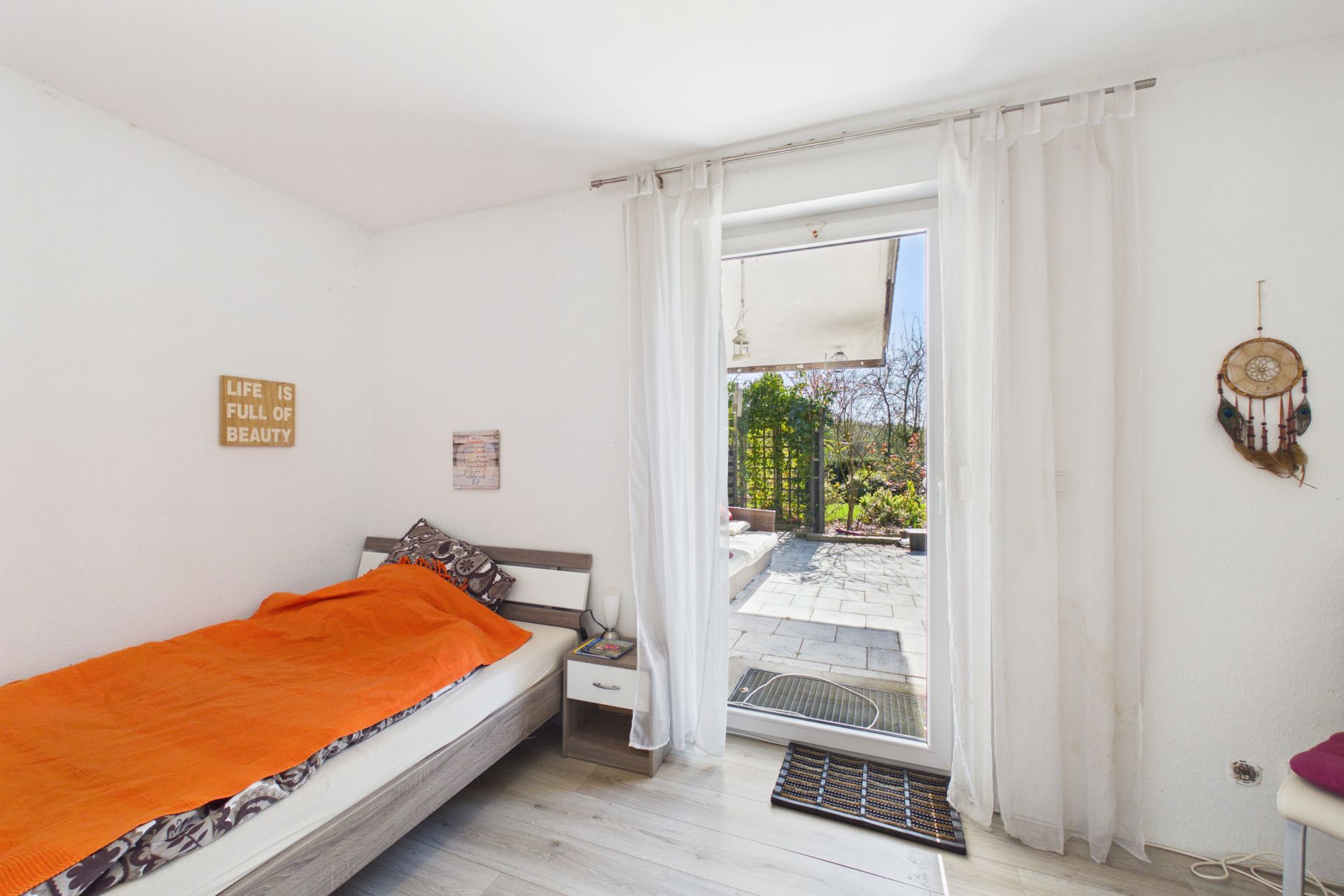 Helles Schlafzimmer mit Einzelbett, orangener Decke und Terrassentür mit Blick nach draußen.