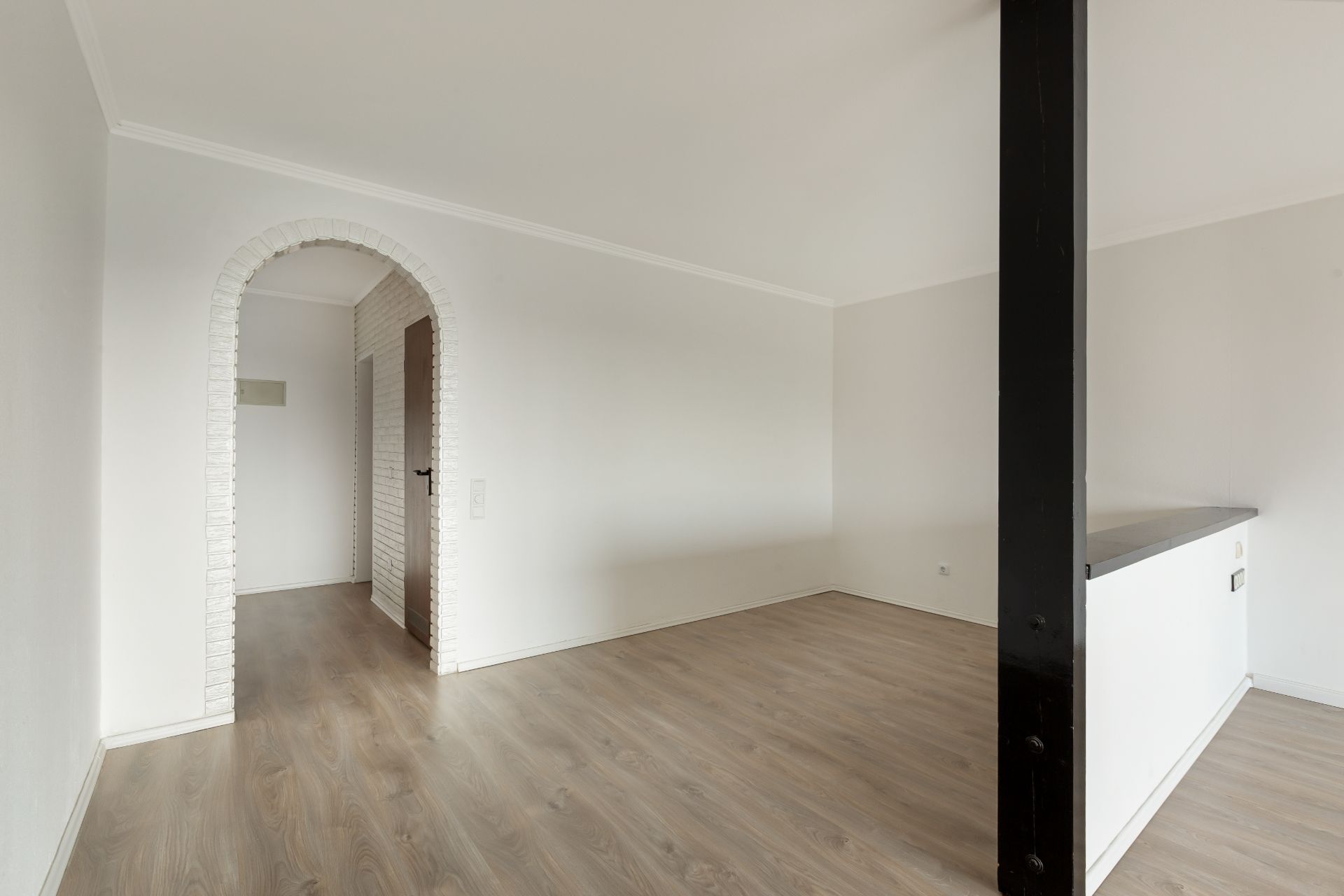 Leeres Zimmer mit Holzboden, weißem Bogen und schwarzer Säule.