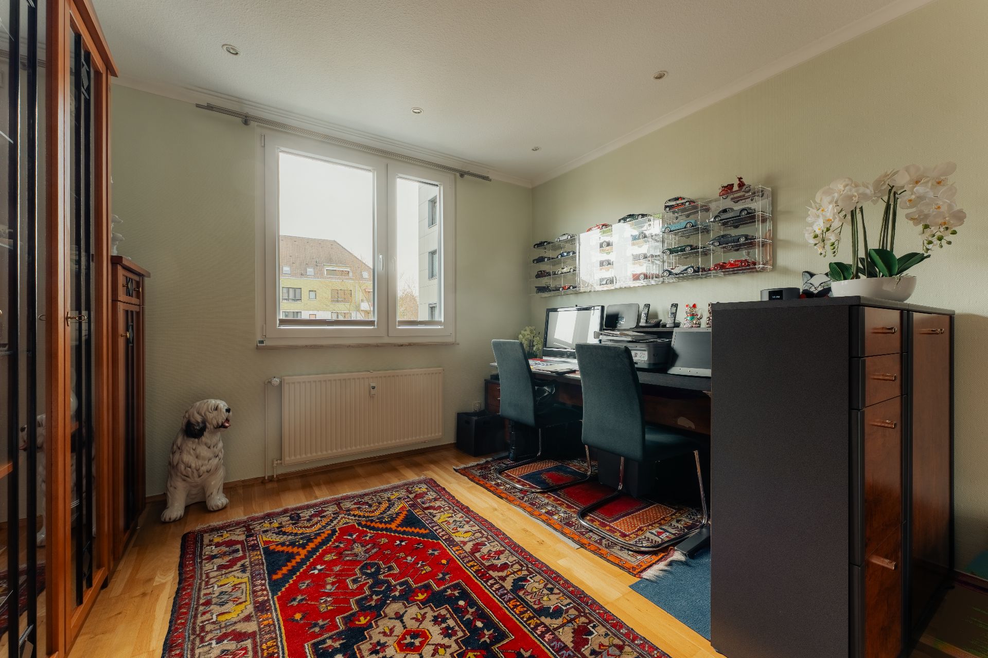 Arbeitszimmer mit zwei Schreibtischen, bunten Teppichen und Regalen mit Modellautos.