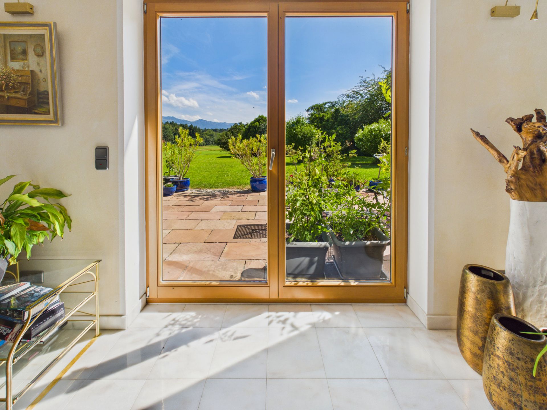 Doppelte Glastür mit Blick auf Terrasse und grünen Garten mit Pflanzen.