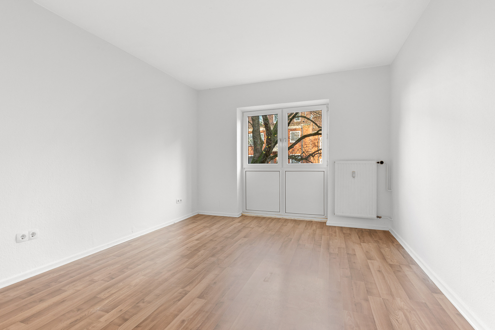 Leerer Raum mit weißen Wänden, Holzfußboden und einem Fenster mit Blick ins Freie.