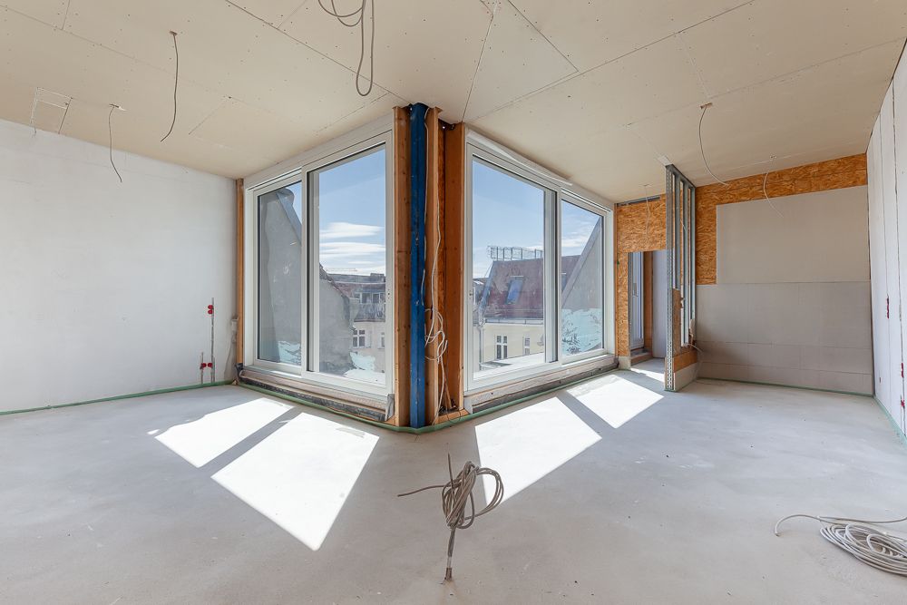 Heller Raum mit großen Fenstern und unfertigen Wänden, sichtbare Kabel an Decke und Boden.
