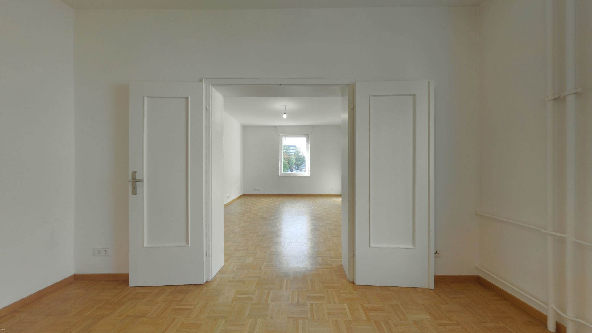 Leerer Raum mit Holzboden, weißen Wänden und Doppeltür zu weiterem Raum mit Fenster.