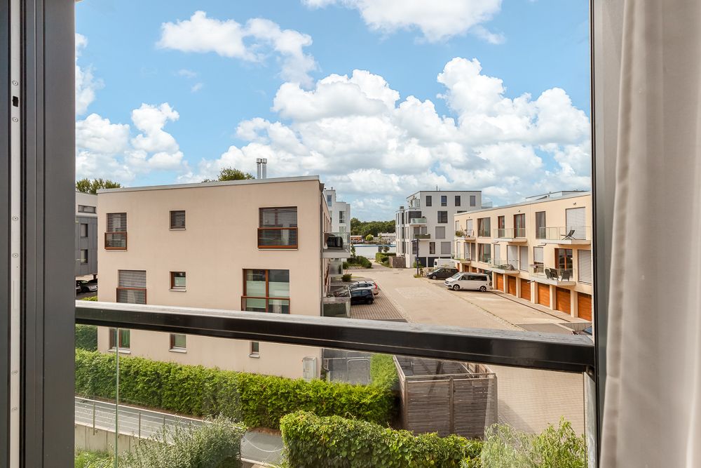 Blick aus dem Fenster auf moderne Wohngebäude und einen Innenhof mit geparkten Autos.