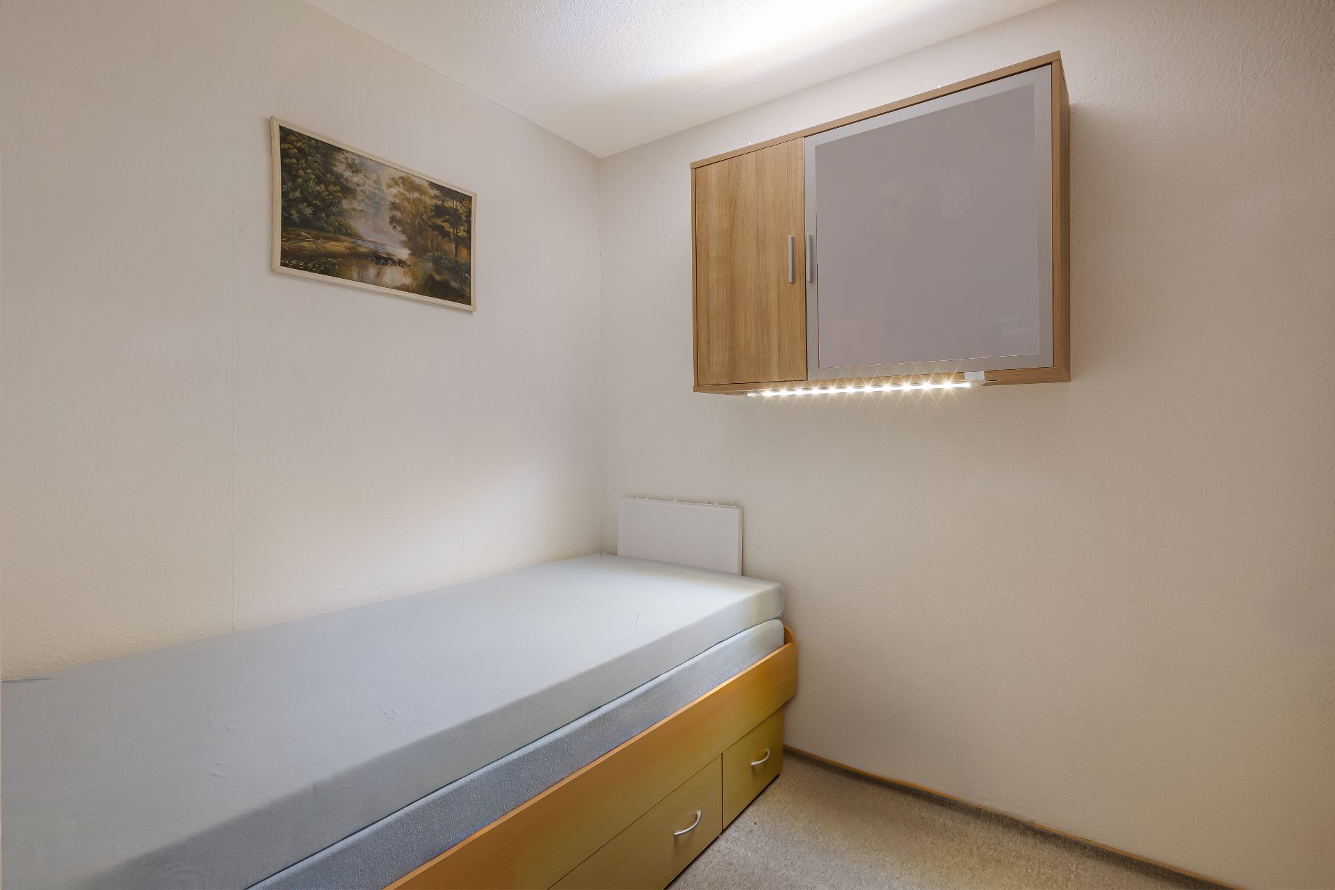 Kleines Schlafzimmer mit Einzelbett, Wandschrank und Bild an der Wand.