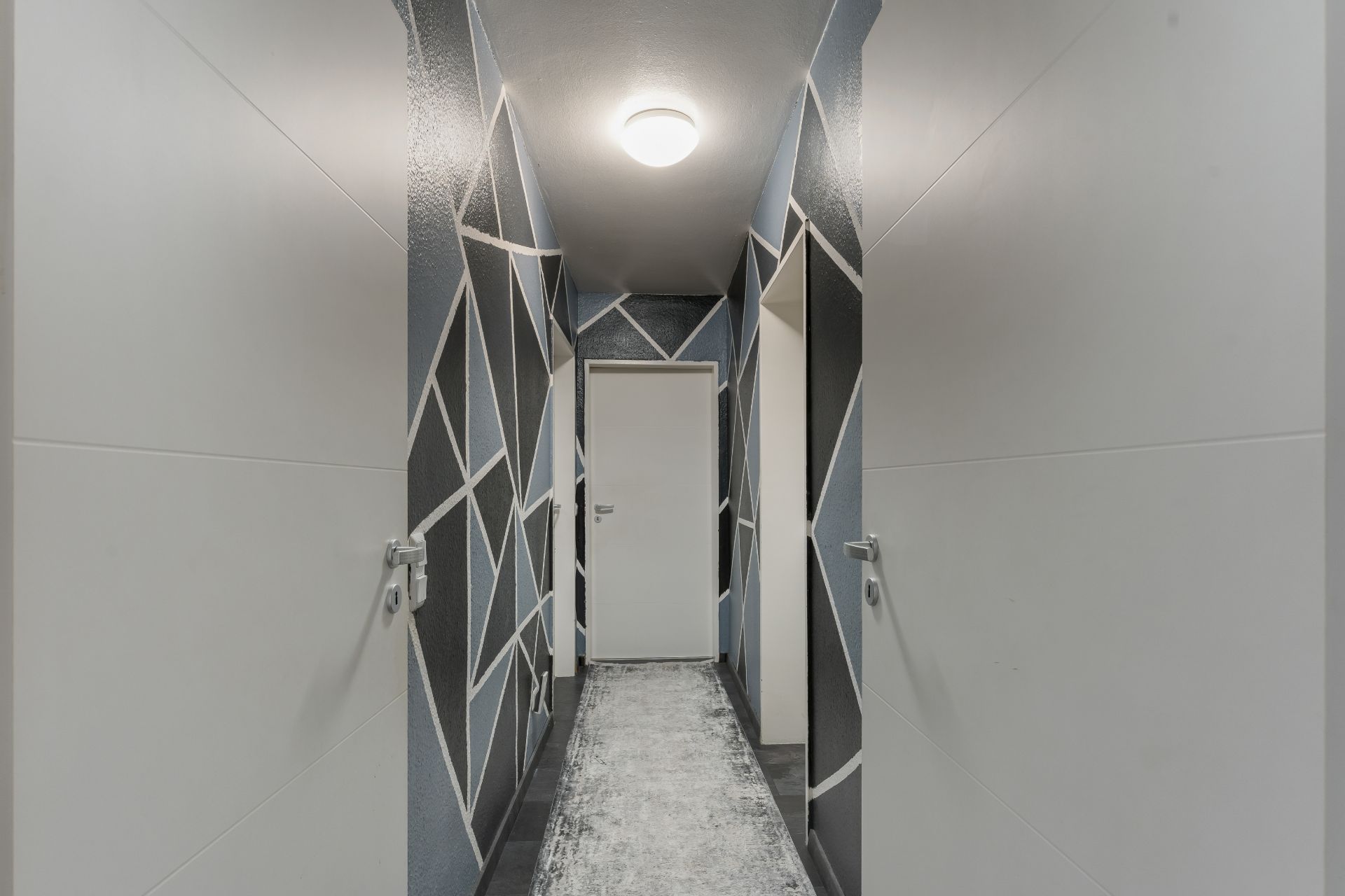 Moderner Flur mit geometrisch gemusterten Wänden, weißen Türen und Teppichläufer.