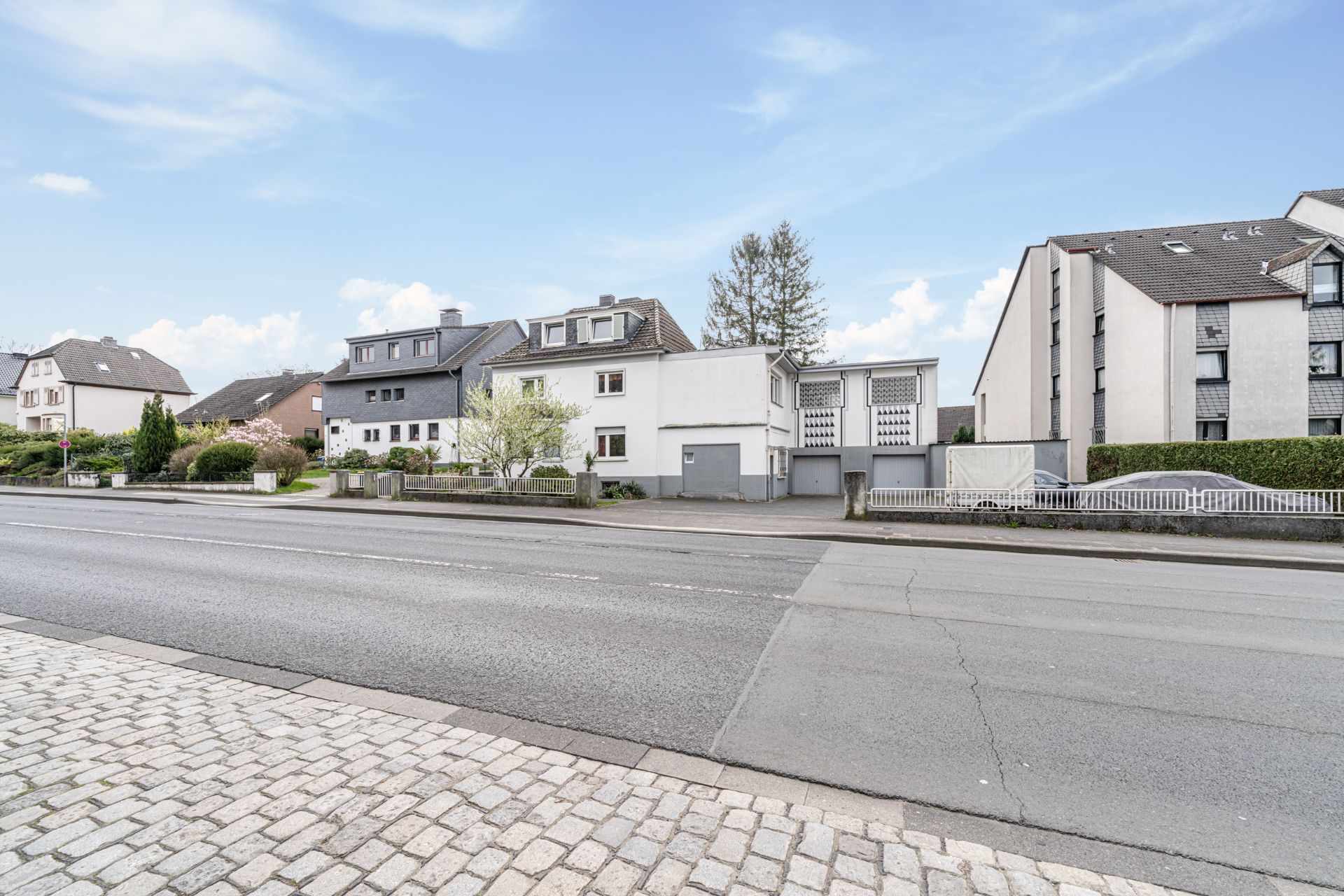 Mehrere Wohnhäuser und Garagen an einer Straße mit Gehweg bei Tageslicht.