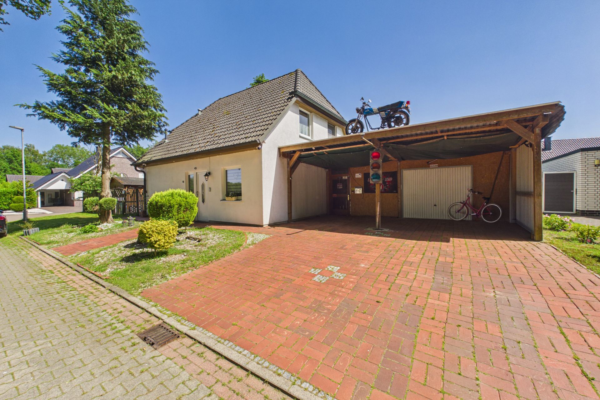 Einfamilienhaus mit Carport, rotem Pflaster und einem Motorrad auf dem Dach des Carports.