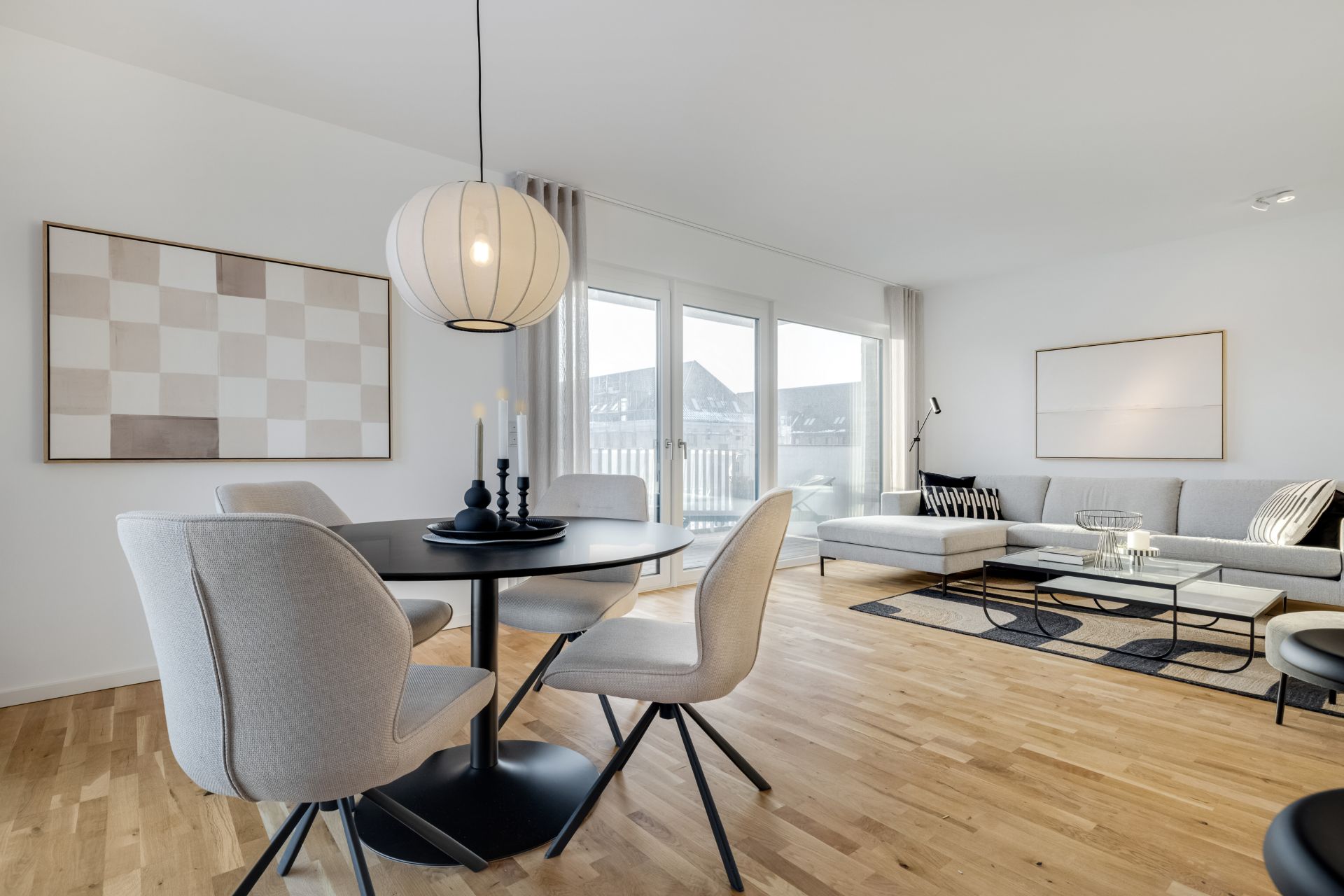 Helles Wohnzimmer mit Esstisch, Stühlen, Sofa und großen Fenstern.