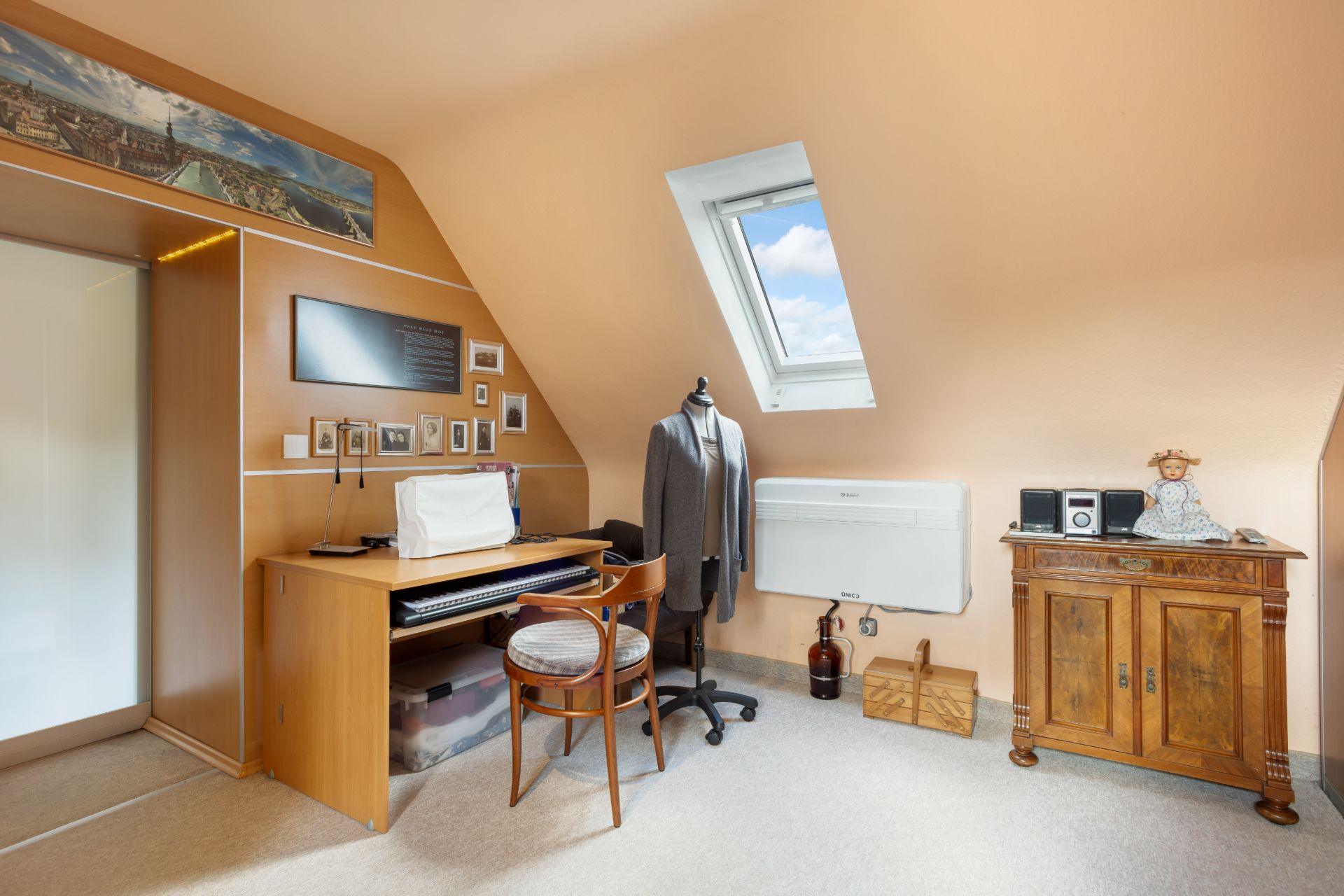 Kleines Arbeitszimmer mit Schreibtisch, Stuhl, Schneiderpuppe und Dachfenster.