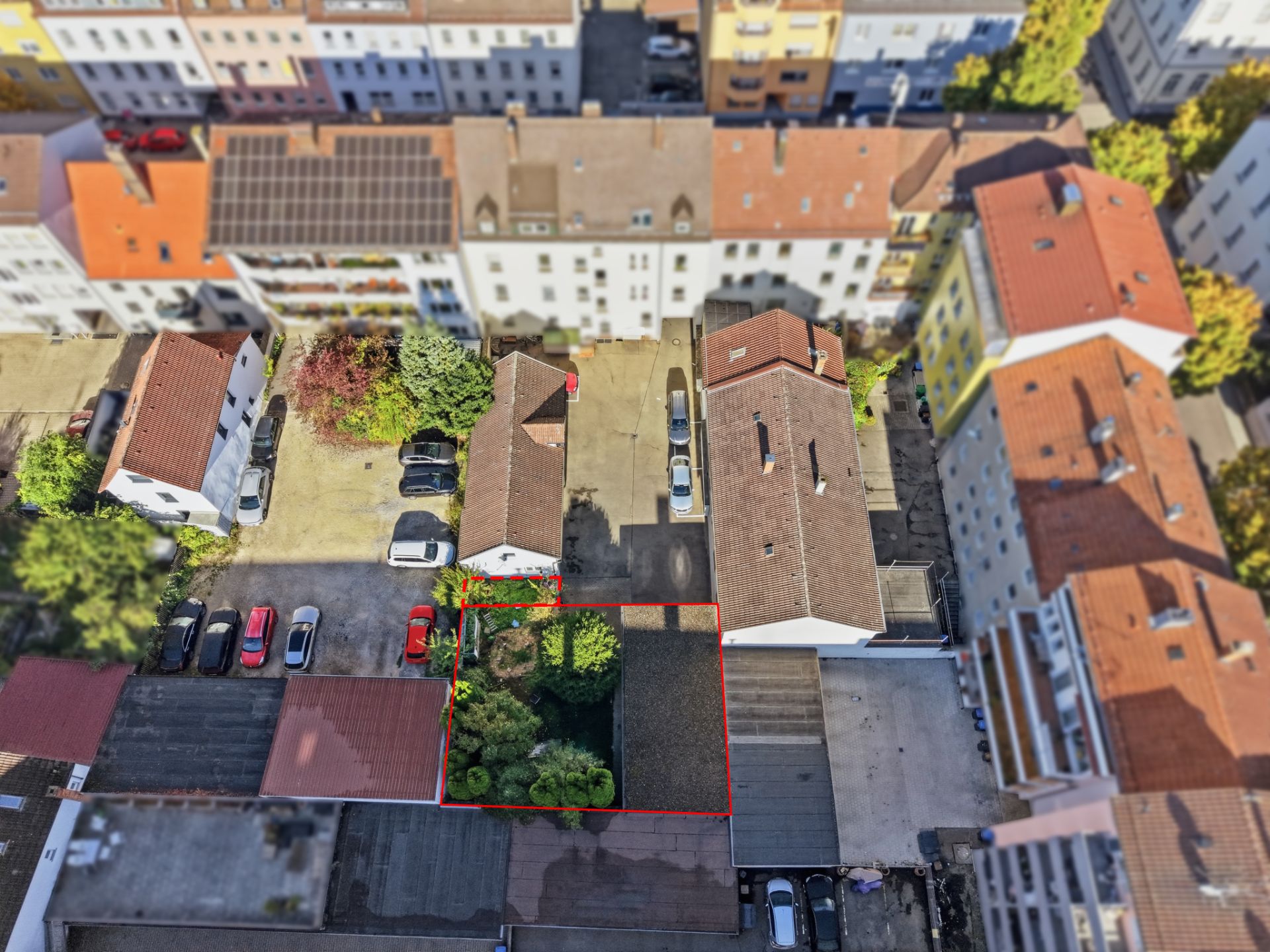 Luftaufnahme eines Hinterhofs mit Garten und Parkplatz, rot umrandet, von Wohnhäusern umgeben.