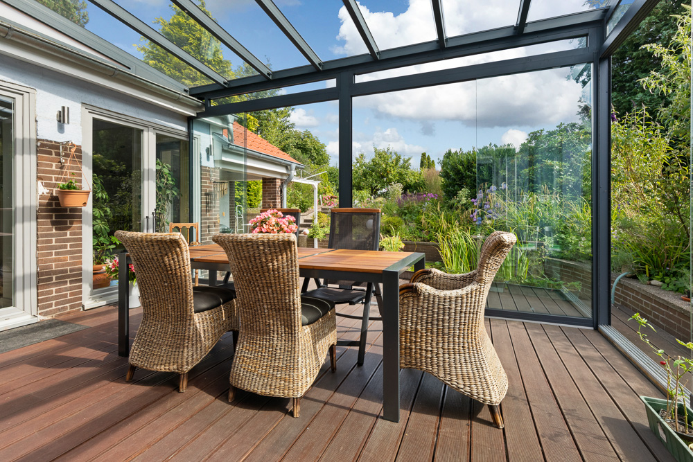 Überdachte Terrasse mit Glastüren, Holzboden, Tisch und vier Korbstühlen, Blick in den Garten.