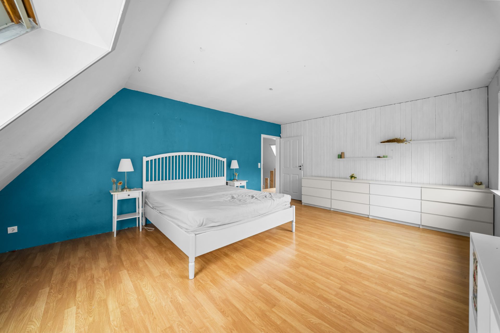 Helles Schlafzimmer mit Holzboden, blau gestrichener Wand, weißem Bett und zwei Nachttischen.