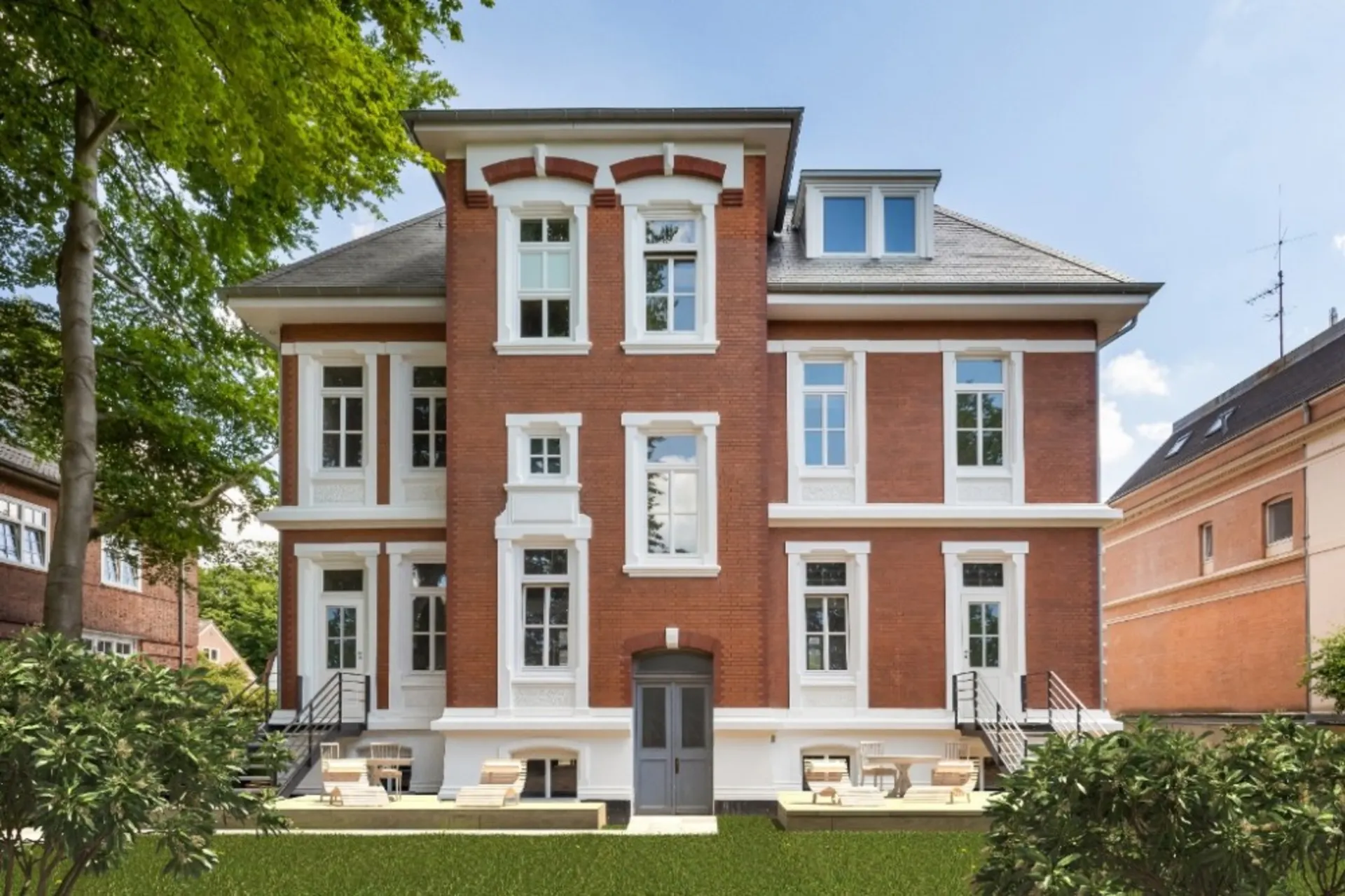 Großes Ziegelhaus mit weißen Fenstereinfassungen, Terrasse und Garten im Vordergrund.