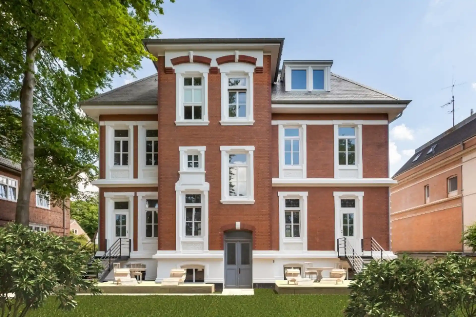 Großes Ziegelhaus mit weißen Fenstereinfassungen, Terrasse und Garten im Vordergrund.