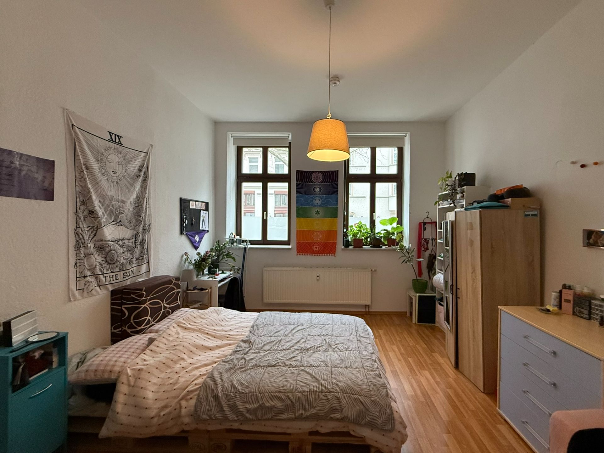 Helles Schlafzimmer mit Doppelbett, Pflanzen am Fenster und bunter Wanddeko.