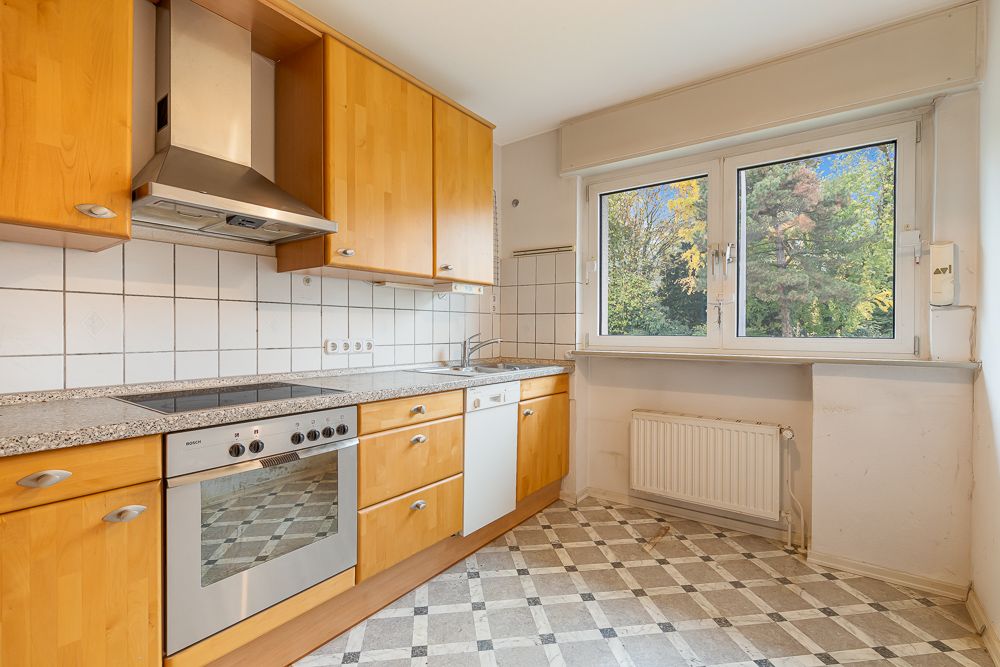 Helle Küche mit Holzschränken, Elektroherd, Dunstabzugshaube und großem Fenster mit Blick ins Grüne.