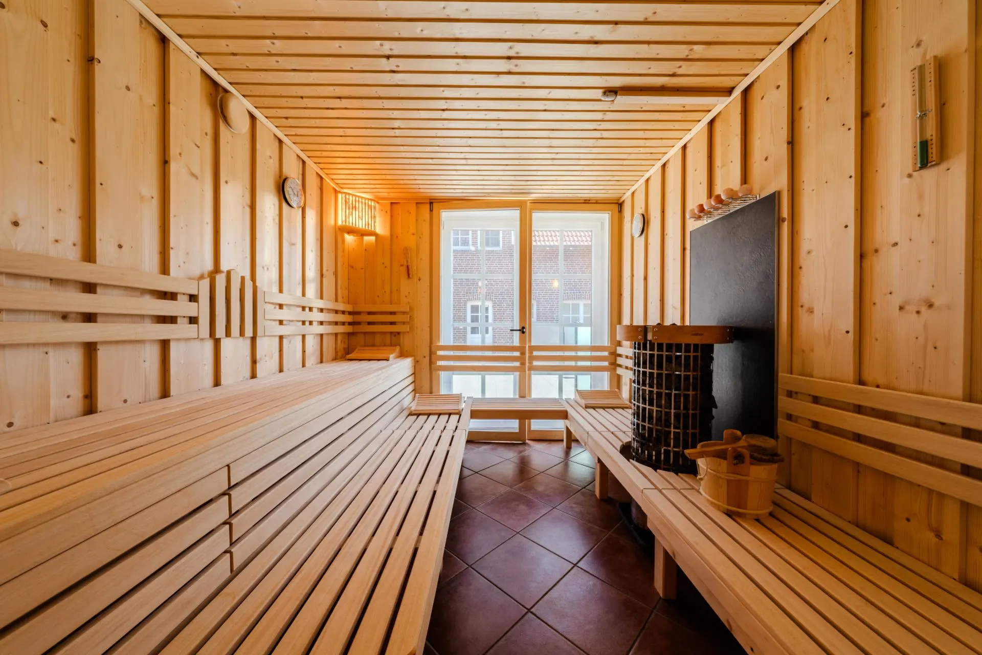 Innenraum einer Sauna mit Holzbänken, Saunaofen und Fenster.