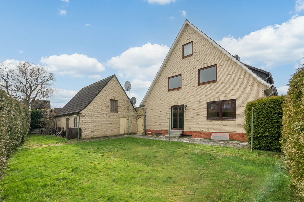Zwei helle Backsteingebäude mit Fenstern, Tür und gepflegtem Garten im Vordergrund.