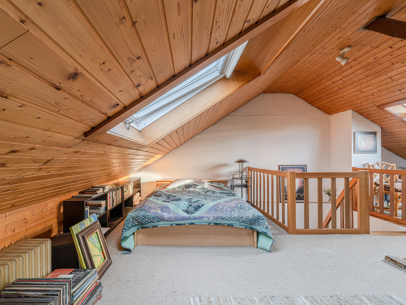 Gemütliches Schlafzimmer im Dachgeschoss mit Holzdecke, Dachfenster und Bücherregal.