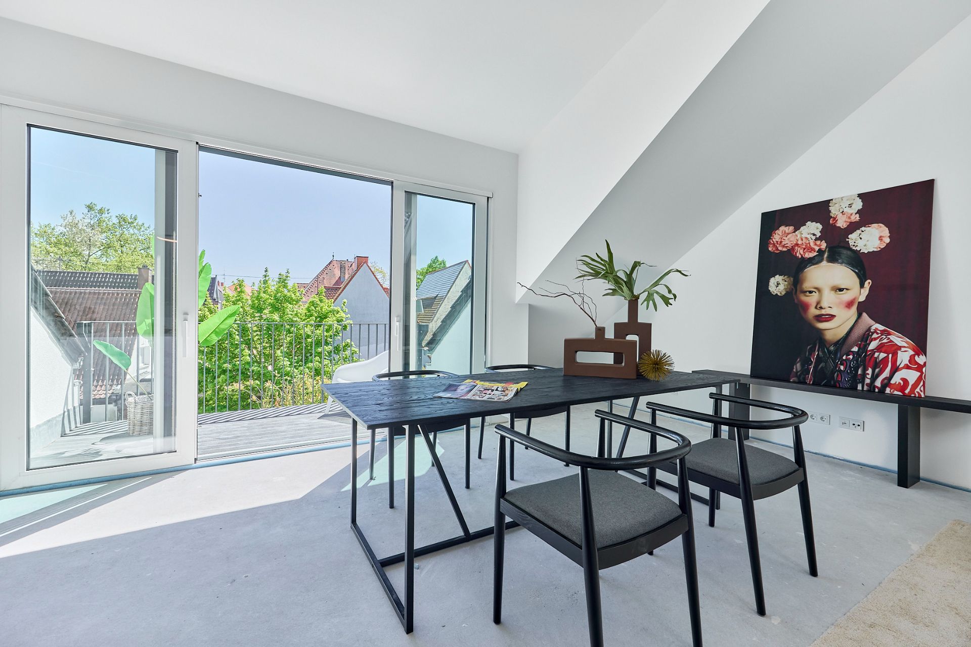 Helles Zimmer mit Schreibtisch, zwei Stühlen, großem Fenster und Pflanzenbild an der Wand.