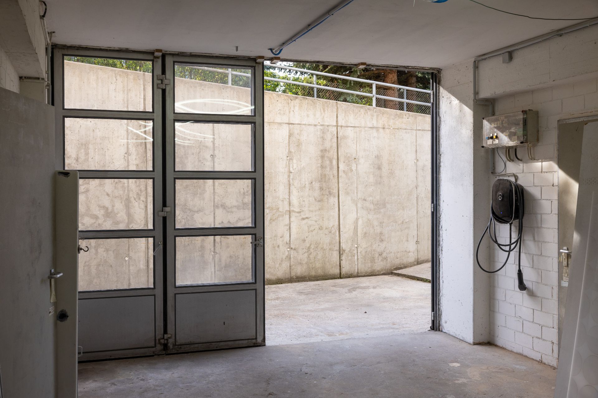 Geöffnete Garage mit Glastür und Blick auf eine Betonauffahrt.