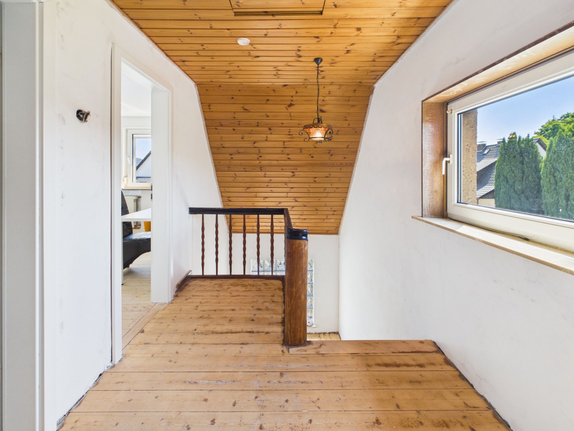 Flur mit Holzfußboden, Holzdecke, Fenster und Treppengeländer in einem Wohnhaus.