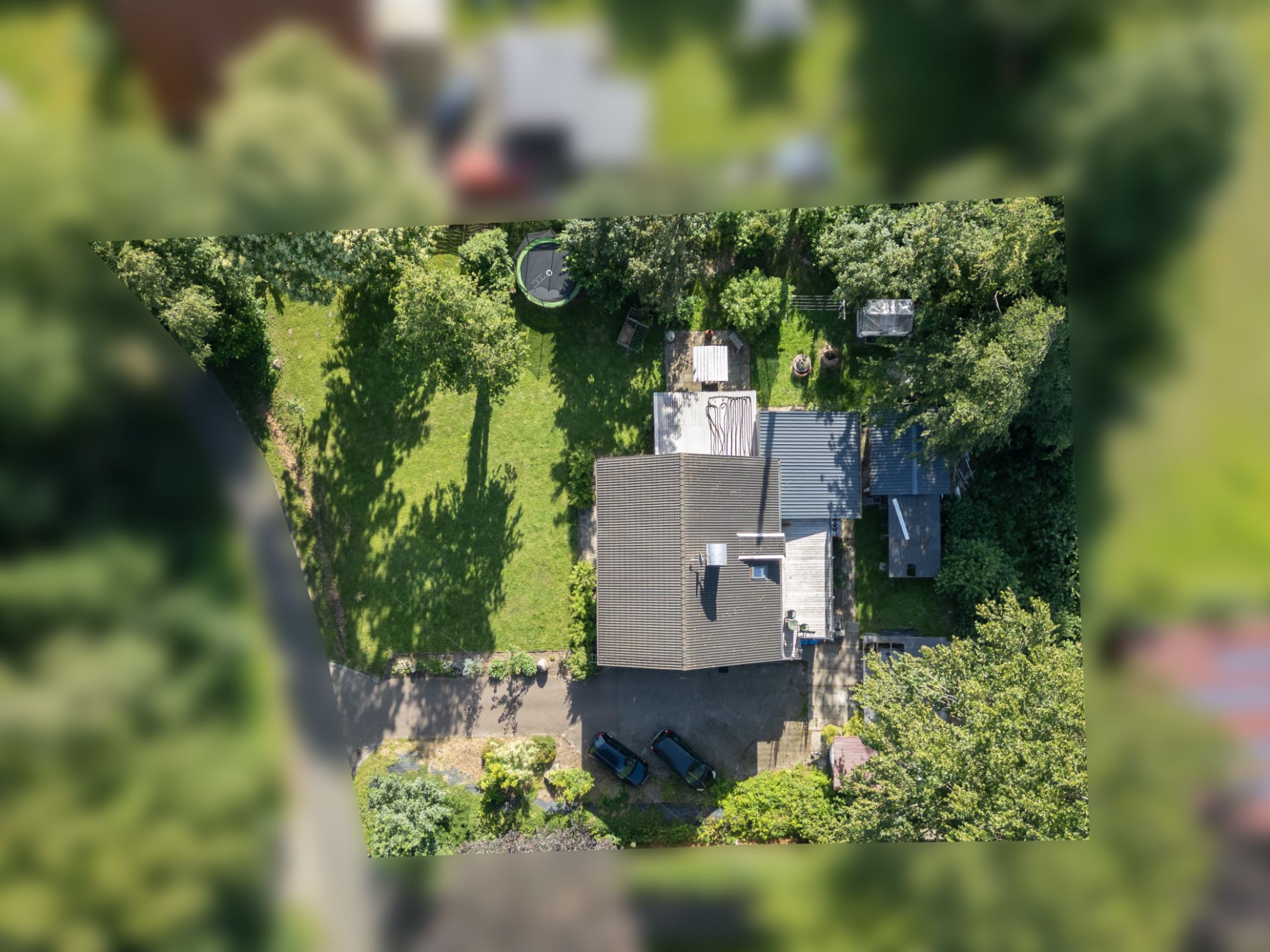 Luftaufnahme eines Hauses mit großem Garten, Auffahrt und Bäumen rundherum.