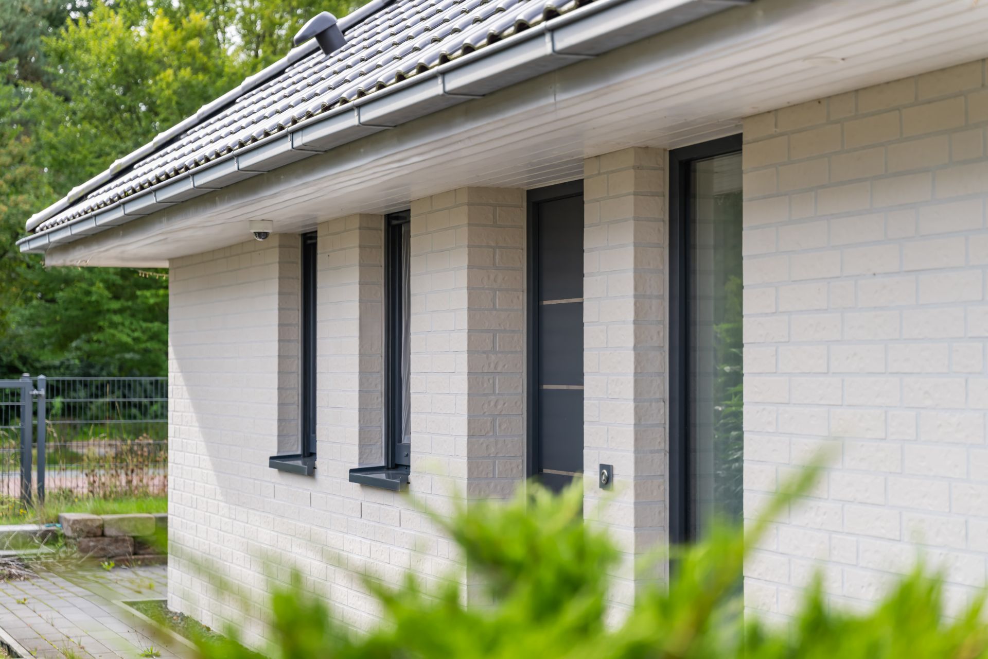 Teilansicht eines modernen Einfamilienhauses mit hellen Ziegelwänden und mehreren Fenstern.