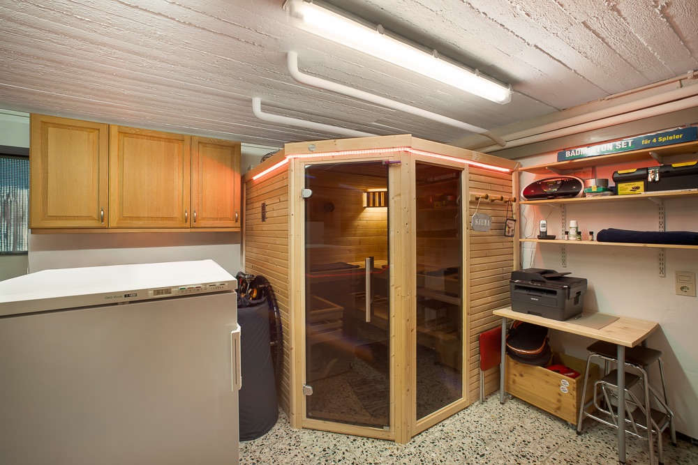 Kellerraum mit Sauna, Gefrierschrank, Holzschränken und Regalen mit verschiedenen Gegenständen.