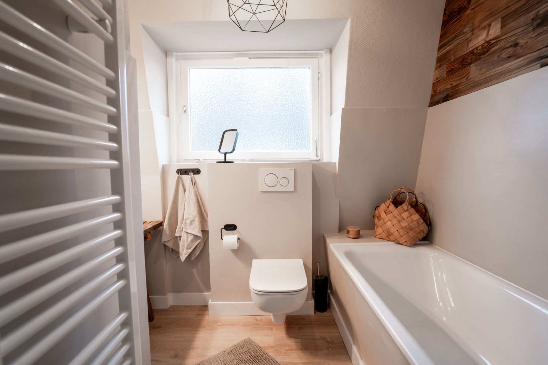 Modernes Badezimmer mit Badewanne, WC, Handtuch, Fenster und Handtuchheizkörper.